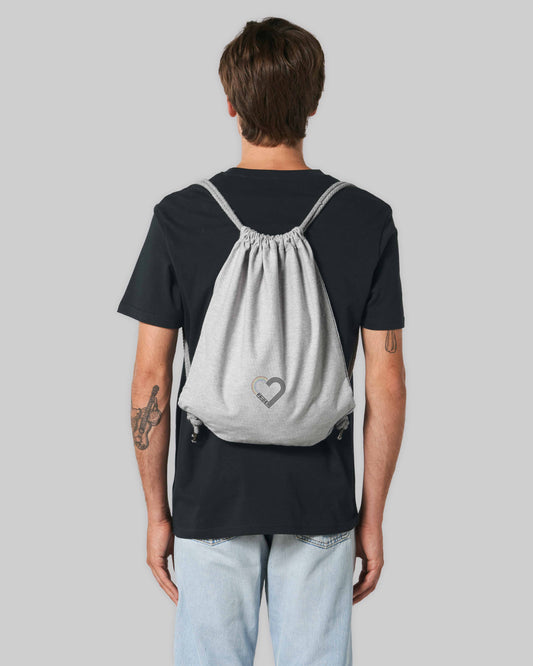 EINHORST® Sportbeutel in "Heather Grey" mit dem Motiv "pride Herz" in der Kombination schwarzer Regenbogen mit schwarzer Schrift, Bild von männlicher Person mit Sportbeutel