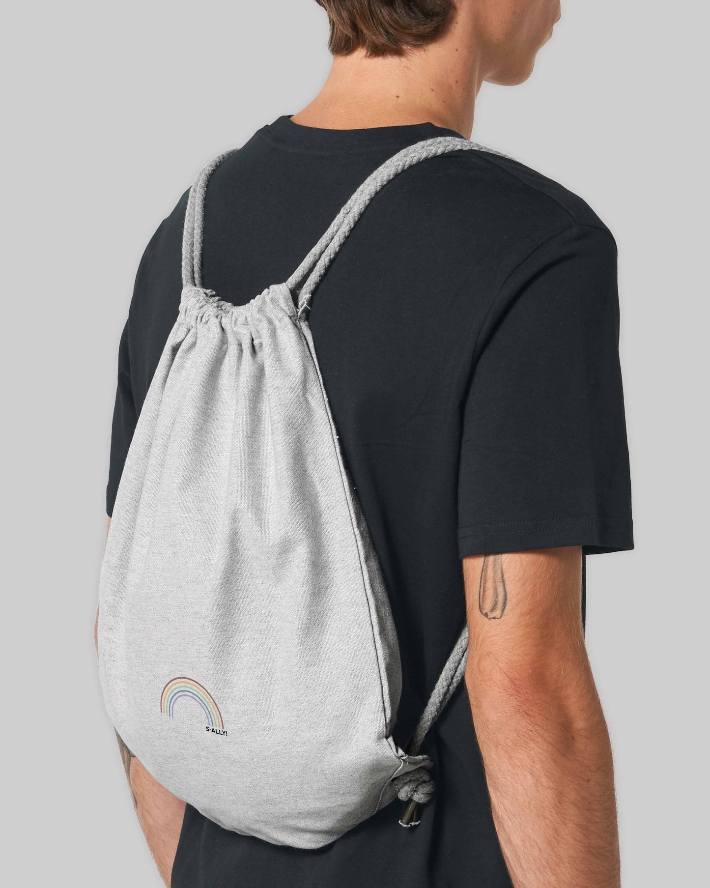 EINHORST® Sportbeutel in "Heather Grey" mit dem Motiv "s-ally Regenbogen" in der Kombination bunter Regenbogen mit schwarzer Schrift, Nahaufnahme von männlicher Person mit Sportbeutel